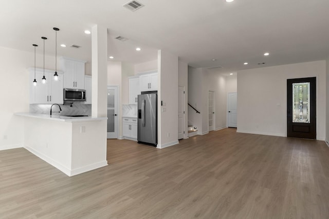 kitchen featuring pendant lighting, white cabinets, light wood-type flooring, kitchen peninsula, and stainless steel appliances