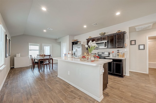 kitchen with appliances with stainless steel finishes, light wood-type flooring, dark brown cabinets, lofted ceiling, and an island with sink