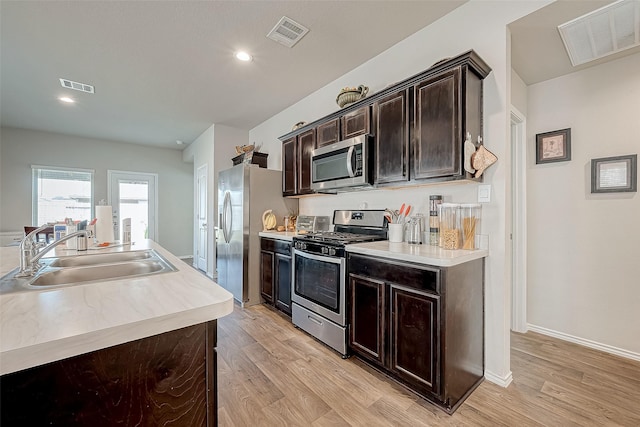 kitchen with a kitchen island with sink, sink, light wood-type flooring, dark brown cabinetry, and stainless steel appliances