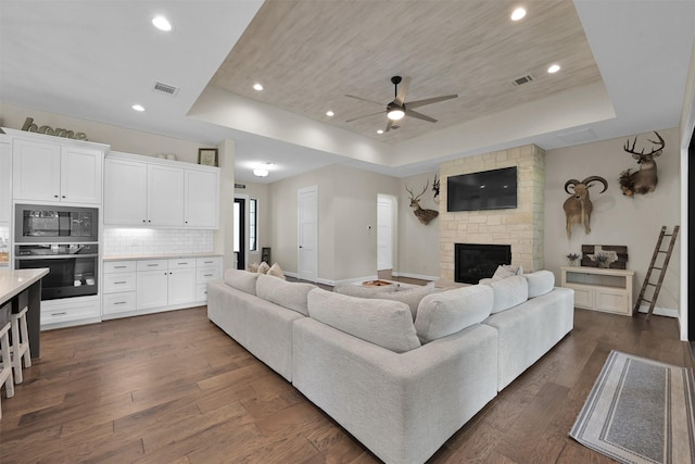 living room featuring a tray ceiling, ceiling fan, a fireplace, and dark wood-type flooring