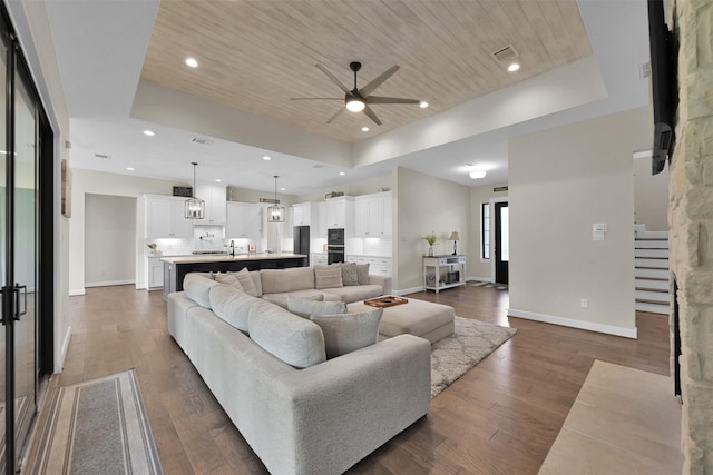 living room with a raised ceiling, ceiling fan, wood ceiling, and dark wood-type flooring