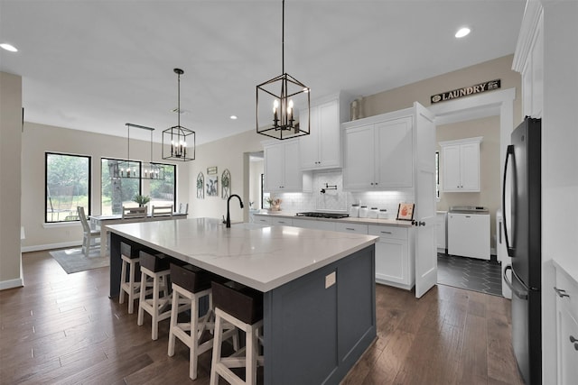 kitchen with dark hardwood / wood-style flooring, a kitchen island with sink, white cabinetry, washer / clothes dryer, and stainless steel refrigerator