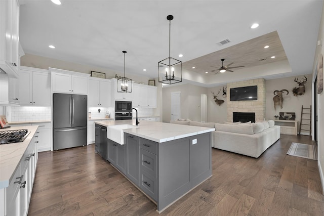 kitchen with a large island with sink, black appliances, white cabinets, a raised ceiling, and dark hardwood / wood-style floors