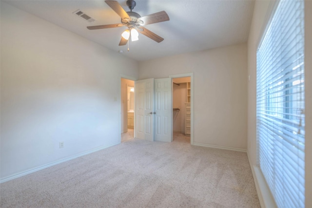 unfurnished bedroom with light carpet, a walk in closet, a closet, and ceiling fan