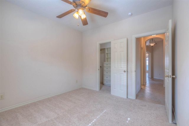 unfurnished bedroom with light carpet, a walk in closet, a closet, and ceiling fan