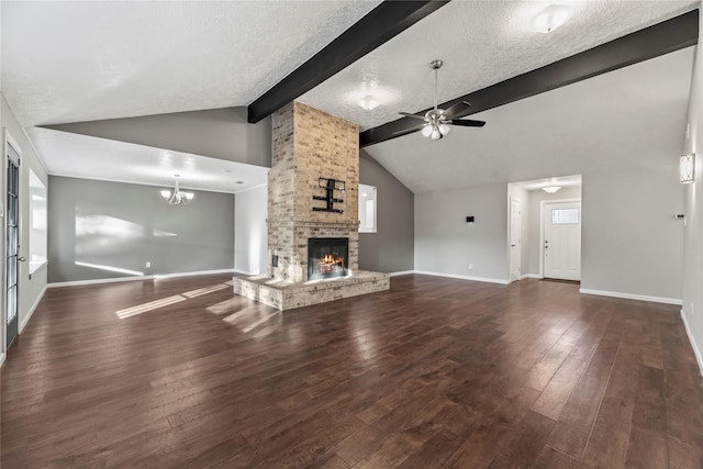 unfurnished living room with a brick fireplace, ceiling fan with notable chandelier, a textured ceiling, dark wood-type flooring, and lofted ceiling with beams