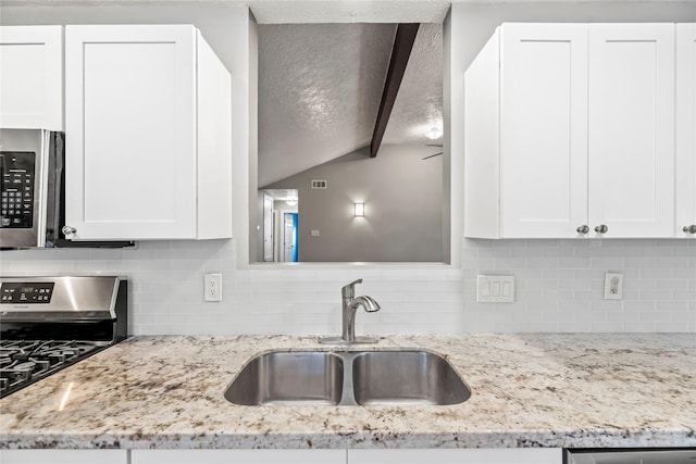 kitchen with sink, lofted ceiling with beams, backsplash, white cabinets, and appliances with stainless steel finishes