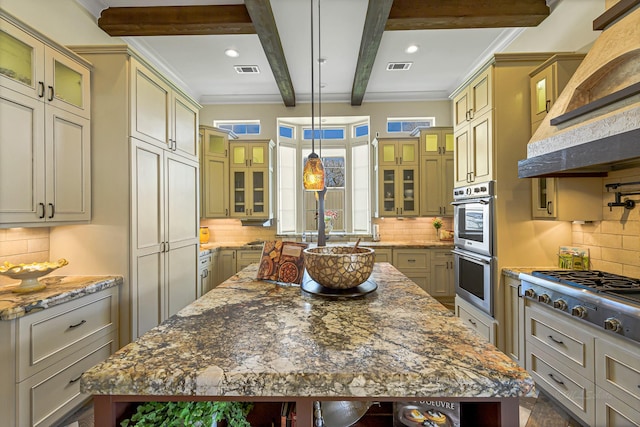 kitchen with light stone countertops, appliances with stainless steel finishes, decorative light fixtures, beamed ceiling, and a center island