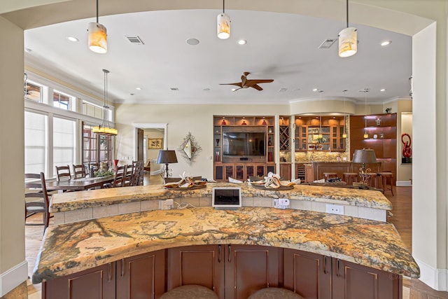 kitchen with ceiling fan, light stone counters, ornamental molding, decorative light fixtures, and light wood-type flooring