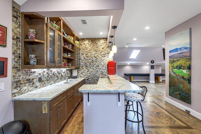 kitchen with light stone countertops, a breakfast bar, hanging light fixtures, and sink