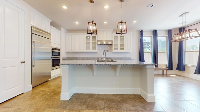 kitchen with pendant lighting, white cabinetry, stainless steel appliances, and a kitchen island with sink