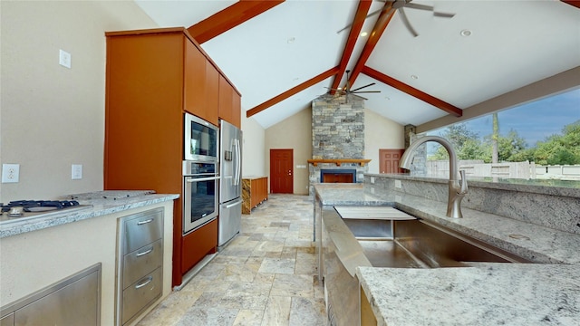 kitchen featuring light stone countertops, appliances with stainless steel finishes, ceiling fan, beamed ceiling, and a fireplace