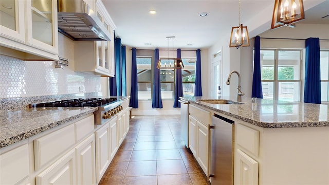 kitchen featuring stainless steel gas cooktop, range hood, backsplash, pendant lighting, and a center island with sink