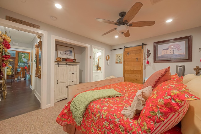 bedroom featuring ceiling fan, a barn door, ensuite bathroom, and dark wood-type flooring