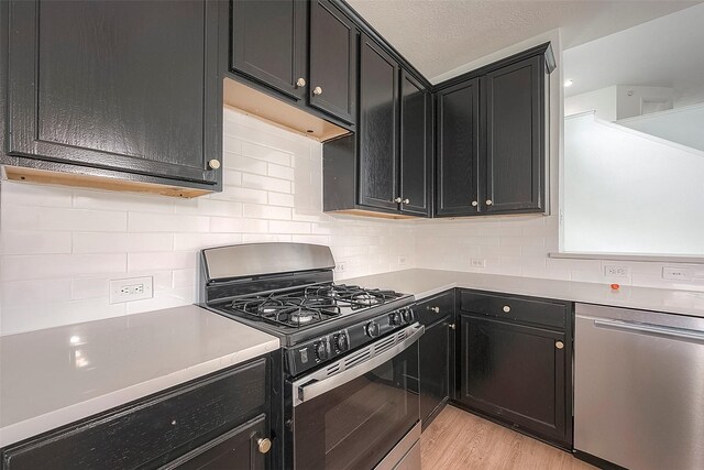 kitchen featuring a textured ceiling, decorative backsplash, light wood-type flooring, and stainless steel appliances