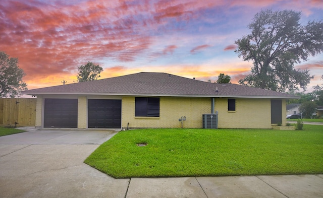 view of front facade featuring central AC, a garage, and a lawn