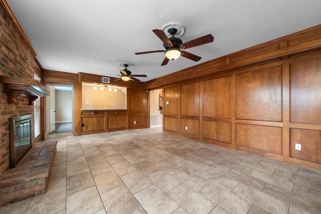 unfurnished living room featuring a fireplace, ceiling fan, and wood walls