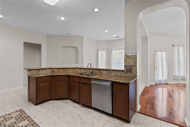 kitchen featuring dishwasher, stone counters, sink, light hardwood / wood-style flooring, and a textured ceiling