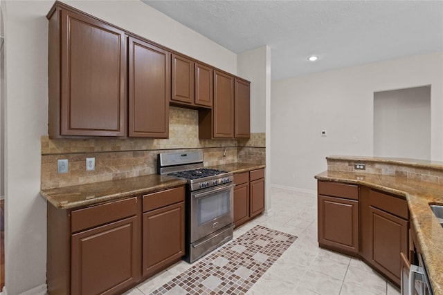 kitchen featuring stainless steel range with gas cooktop, decorative backsplash, light tile patterned floors, a textured ceiling, and light stone counters