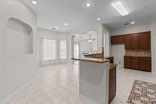 kitchen featuring backsplash, ceiling fan, an island with sink, and a textured ceiling