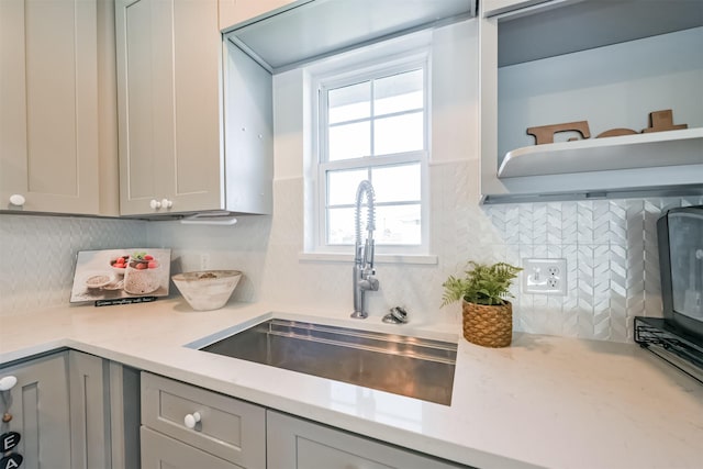 kitchen with decorative backsplash, gray cabinets, light stone counters, and sink