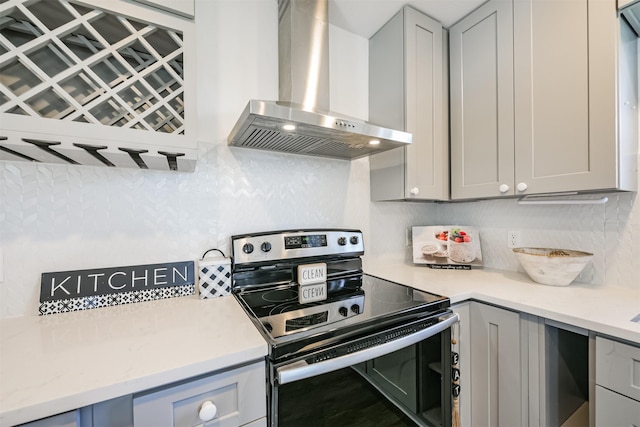 kitchen featuring wall chimney exhaust hood, gray cabinets, decorative backsplash, and stainless steel electric range oven