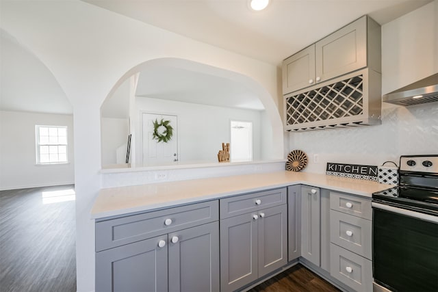 kitchen featuring gray cabinetry, electric range, dark wood-type flooring, wall chimney range hood, and backsplash