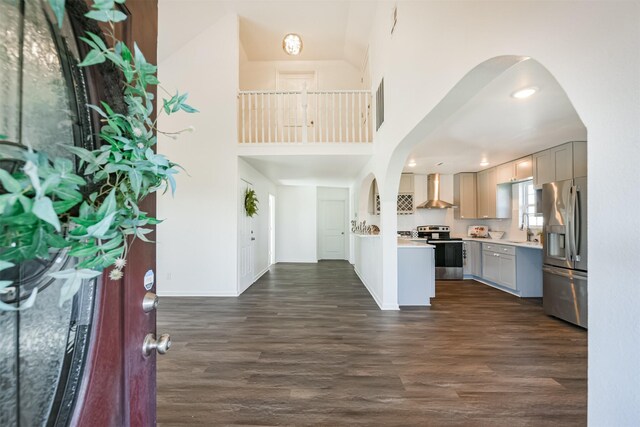 kitchen with dark hardwood / wood-style flooring, stainless steel appliances, sink, wall chimney range hood, and a high ceiling