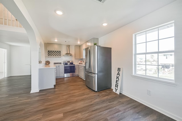 kitchen with decorative backsplash, dark hardwood / wood-style floors, wall chimney range hood, and appliances with stainless steel finishes