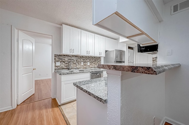 kitchen featuring stone counters, decorative backsplash, light wood-type flooring, white cabinetry, and stainless steel appliances