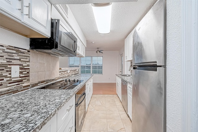 kitchen featuring light stone counters, backsplash, a textured ceiling, white cabinets, and black appliances