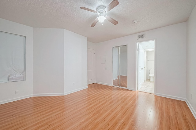 unfurnished bedroom featuring ceiling fan, light hardwood / wood-style floors, a textured ceiling, and connected bathroom