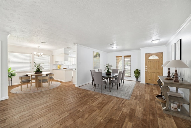 dining space featuring a textured ceiling, light hardwood / wood-style flooring, crown molding, and a notable chandelier