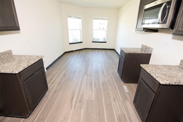 kitchen with light stone counters, dark brown cabinets, and light wood-type flooring