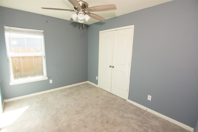 unfurnished bedroom with a closet, light colored carpet, multiple windows, and ceiling fan