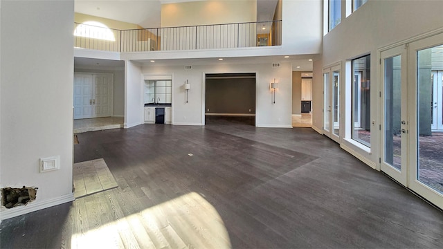 unfurnished living room featuring french doors, sink, dark wood-type flooring, and a high ceiling