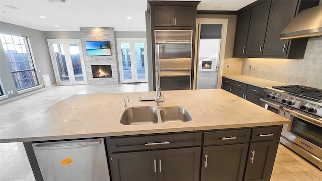 kitchen featuring a wealth of natural light, ventilation hood, a kitchen island with sink, sink, and high quality appliances