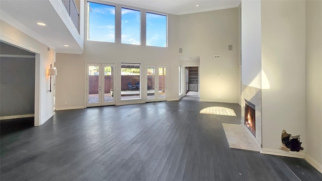 unfurnished living room featuring a high ceiling, dark hardwood / wood-style flooring, french doors, and a tiled fireplace