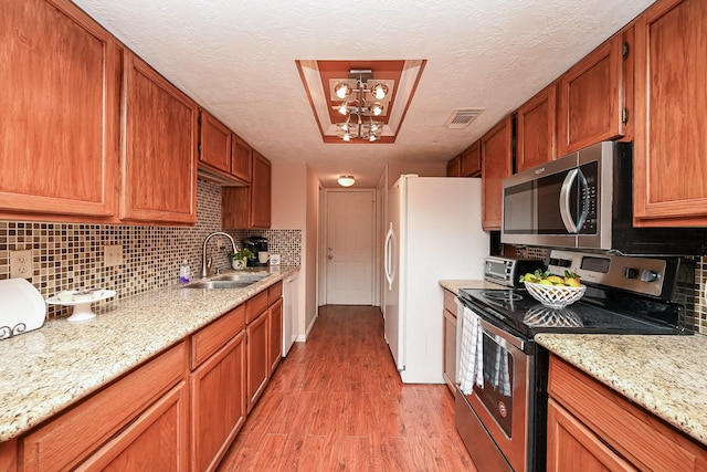 kitchen with sink, a textured ceiling, appliances with stainless steel finishes, tasteful backsplash, and light hardwood / wood-style floors