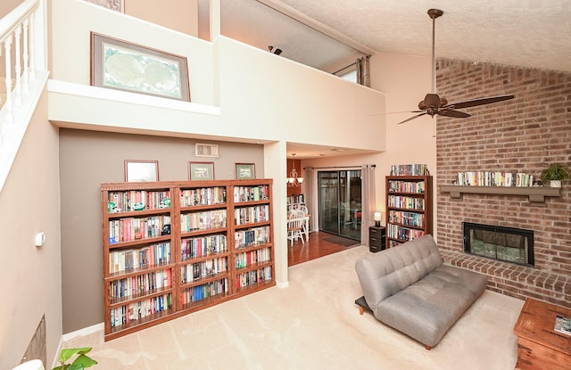 sitting room with carpet flooring, a brick fireplace, high vaulted ceiling, a textured ceiling, and ceiling fan with notable chandelier