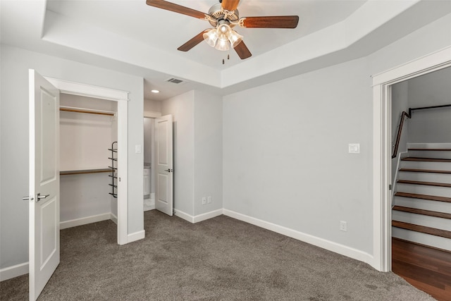 unfurnished bedroom featuring a tray ceiling, ceiling fan, a closet, and dark colored carpet