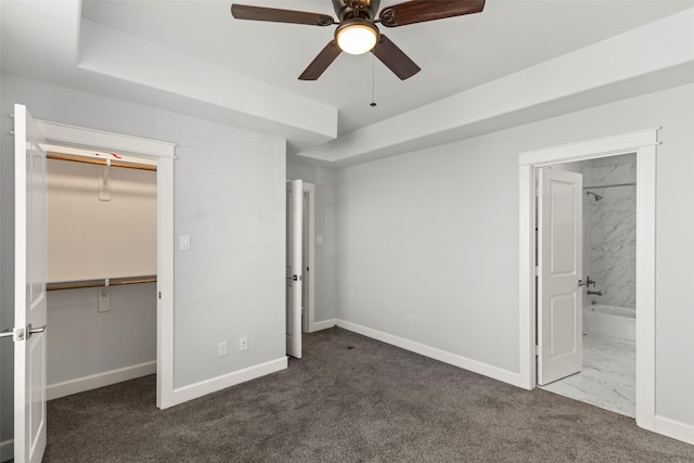 unfurnished bedroom featuring dark colored carpet, connected bathroom, a closet, and ceiling fan