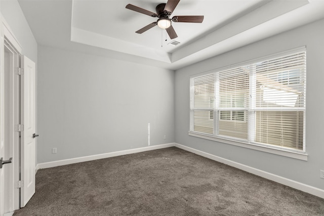 unfurnished room with ceiling fan, dark carpet, and a tray ceiling