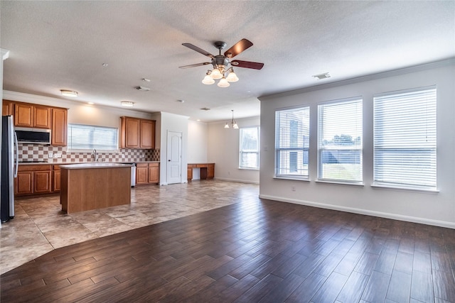 kitchen featuring backsplash, crown molding, light wood-type flooring, a kitchen island, and stainless steel appliances