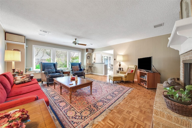 living room with wood walls, a brick fireplace, ceiling fan, a textured ceiling, and light parquet flooring