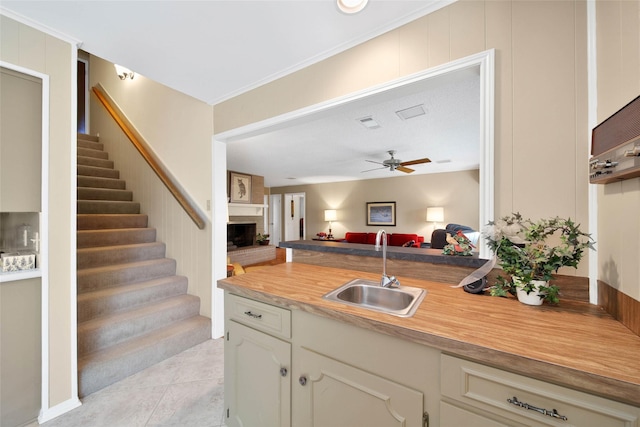 kitchen with sink, ceiling fan, ornamental molding, a fireplace, and light tile patterned flooring