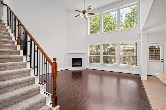 unfurnished living room with ornate columns, ceiling fan, a high ceiling, a premium fireplace, and wood-type flooring