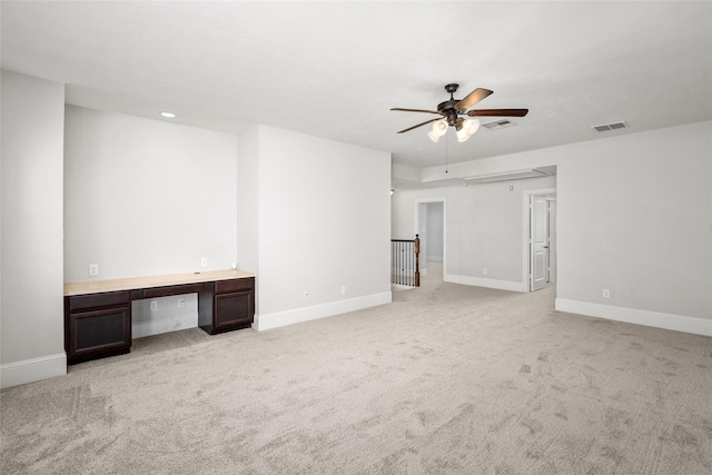 spare room with light carpet, ceiling fan, and built in desk