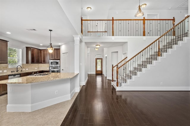 kitchen featuring appliances with stainless steel finishes, tasteful backsplash, light stone counters, wood-type flooring, and decorative light fixtures