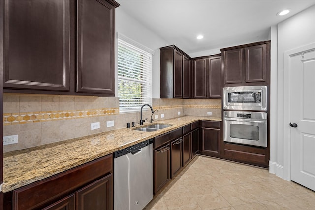 kitchen featuring dark brown cabinetry, sink, light stone counters, decorative backsplash, and appliances with stainless steel finishes